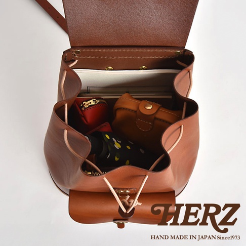 職人手作皮革經典後背包 R-4，以棕色皮革製成，包款內裝有紅色的零錢包、棕色的皮夾、一本筆記本和一把印有黃色花朵圖案的摺疊傘。