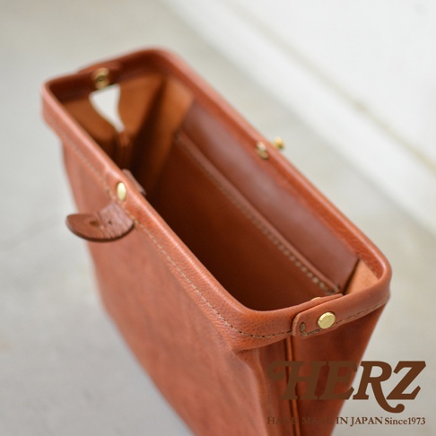 職人手作皮革Organ手拿包，呈現暖棕色調，以皮革材質製作，包身結構穩固，內有隔層，並以金屬釦件固定。