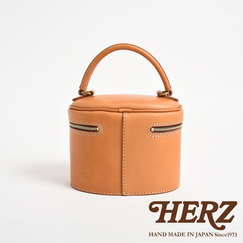 職人手作皮革圓筒型化妝手提包，淺棕色，圓潤造型，頂部有提把，側邊有拉鍊開口，適合收納化妝品。