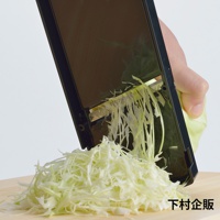 手持黑色超薄切高麗菜刨絲器，正在刨切新鮮高麗菜，刨出的細絲堆疊成一堆。