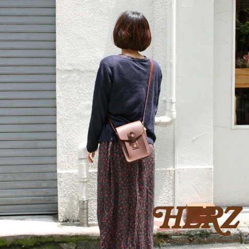 一位女士背著一個棕色皮革製成的斜背包，包包上有金屬扣環和縫線細節。