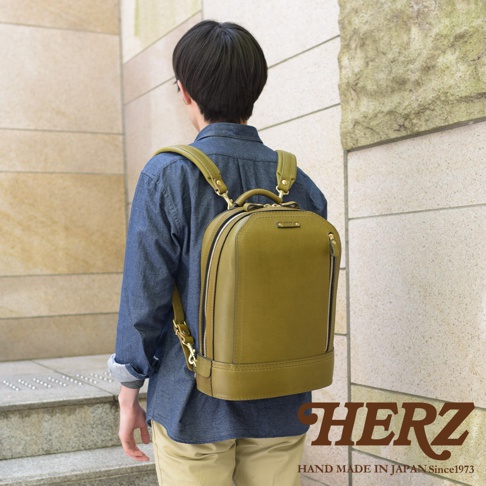 一名男子身背一個橄欖綠色的立體皮革商務後背包，背包側面有拉鍊，頂部有提把，肩帶為可調節式。