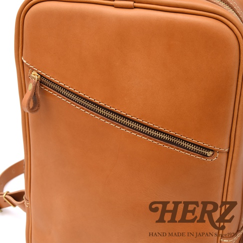 職人手作皮革後背包，採用天然皮革，呈現溫潤的棕褐色，設計簡約，搭配斜向拉鍊口袋與精緻縫線，質感細膩。