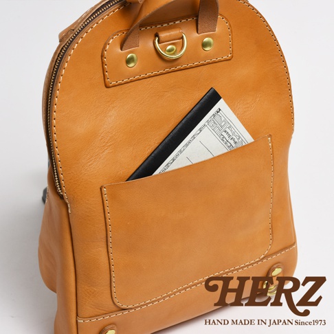 職人手作皮革大開口圓角後背包，採用天然皮革材質，呈現溫潤的焦糖棕色。包款設計有外置口袋，可放入筆記本，並配有金屬拉鍊及D型環。