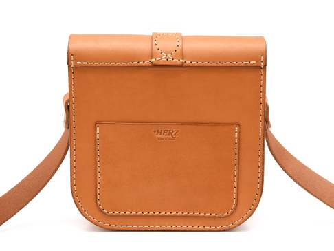 棕褐色皮革製作的單肩包，包身有方形前袋，袋口處有帶扣，並以白色縫線裝飾，整體風格簡約。