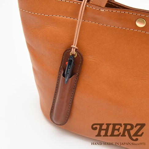 一個棕色皮革手提包，上面掛著一個較小的棕色皮革筆套，裡面插著一支筆。