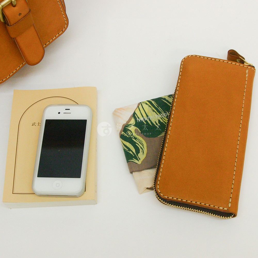 職人手作皮革長夾，焦糖色，拉鍊開合，內含手機、書本與印花布料。