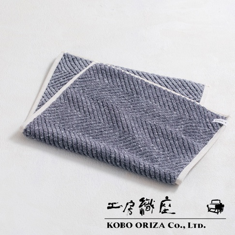 藍灰色棉麻混紡人字紋浴墊，邊緣有白色滾邊。