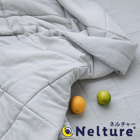 淺灰色菱格紋單人被，表面平整，材質輕柔。一橘黃色檸檬和一綠色萊姆置於被子上，品牌Logo置於右下角。