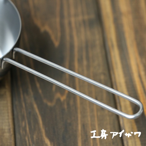 不鏽鋼長柄量杯，銀色，具有兩個平行的長柄，放在木質背景上。