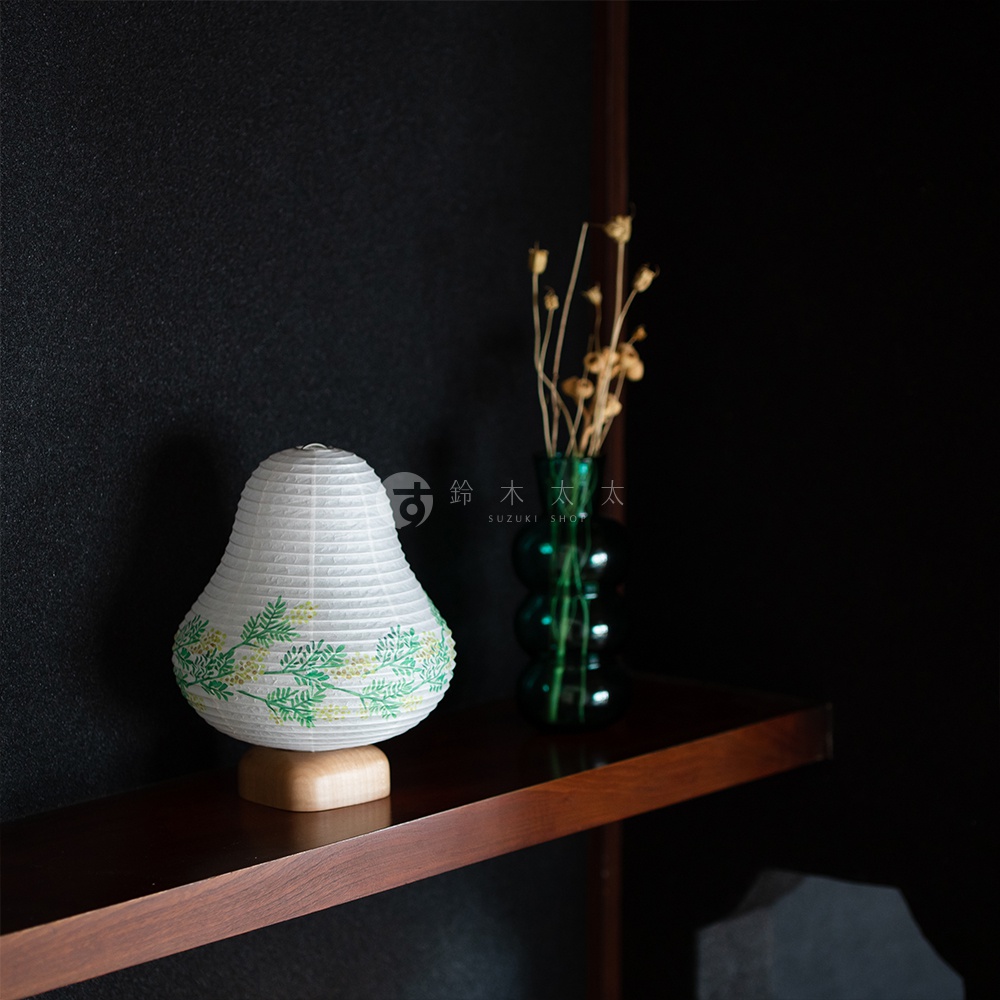 白色日式紙燈，底部為木質座，燈身飾有綠色枝葉與黃色小花圖案，整體呈現梨形。