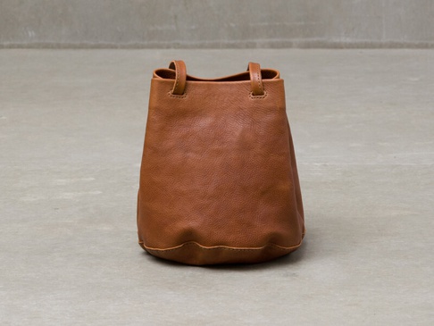 棕色皮革抽繩水桶包，附有兩個短提把，包身圓潤，底部有縫線細節，整體呈現簡約設計。