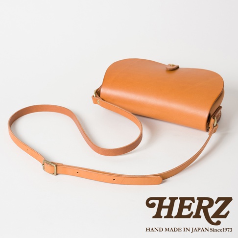 職人手作皮革迷你馬鞍包，採用天然棕色皮革製成，包身呈現圓潤的曲線，配有可調節長度的皮革背帶和銅色金屬釦。