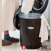 OBAKETSU 標誌的棕色金屬垃圾桶，人們正把白色的衣物丟進去。