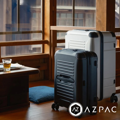 兩款 AZPAC Trucker 2.0 20吋行李箱，一款為霧面黑色，另一款為白色，皆為硬殼材質，表面有橫向紋路設計，配有煞車輪與拉桿。