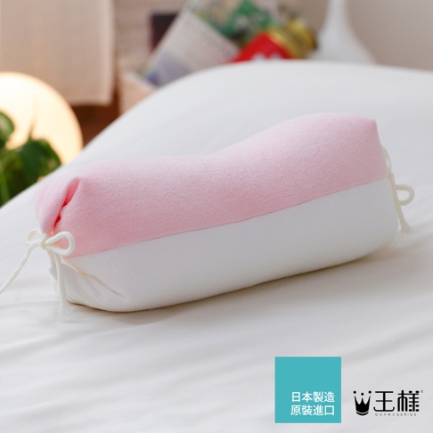 一個粉紅色和白色的糖果形狀枕頭，枕頭兩端有白色綁繩，材質看起來柔軟，放置在白色床單上。