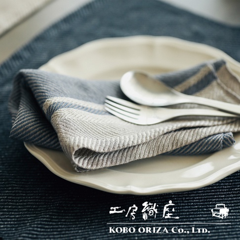 一條淺灰色與藍色條紋的純亞麻斜紋萬用廚房拭巾，疊放在白色盤子上，並配有銀色湯匙和叉子。