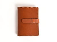 職人手作皮革卡片收納夾，採用光滑的淺棕色皮革製成，帶有可調節的皮革腰帶閉合設計，邊緣縫線整齊，整體呈長方形，經典實用。