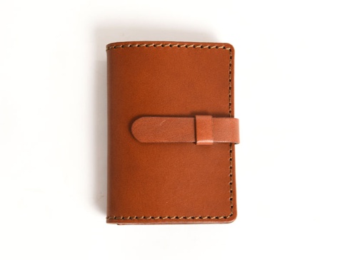 職人手作皮革卡片收納夾，採用光滑的淺棕色皮革製成，帶有可調節的皮革腰帶閉合設計，邊緣縫線整齊，整體呈長方形，經典實用。