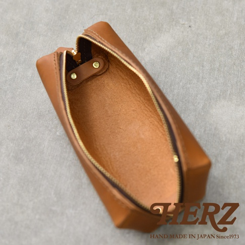 職人手作皮革Organ箱型收納筆袋，採用鞣製皮革製成，呈現自然的棕褐色。筆袋為箱型設計，開口處有金色拉鍊，內側有皮革固定片和金屬卯釘。