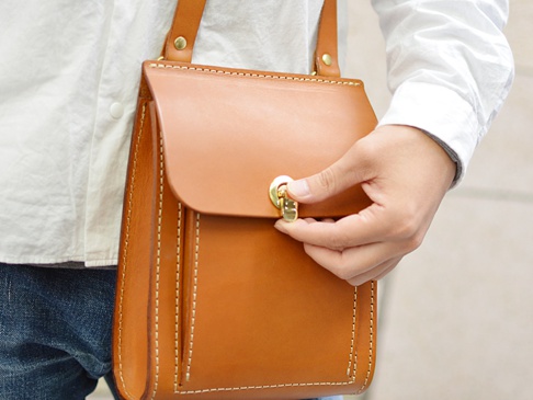 職人手作厚實皮革單肩包，棕褐色皮革，帶有金色旋轉鎖扣，縫線清晰。