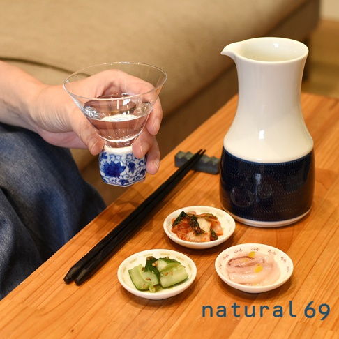 手繪風小菜碟，白色陶瓷，飾有藍色花紋，盛有醃黃瓜、泡菜及魷魚。旁邊擺放一對黑色筷子和一個藍白相間的酒器。