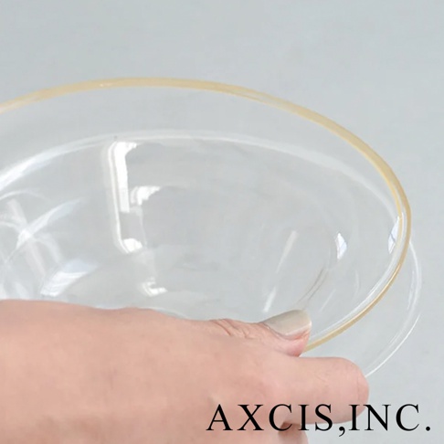 手持一個透明玻璃材質的深型點心碗，碗緣帶有淺金色飾邊，碗身映照出環境光源。