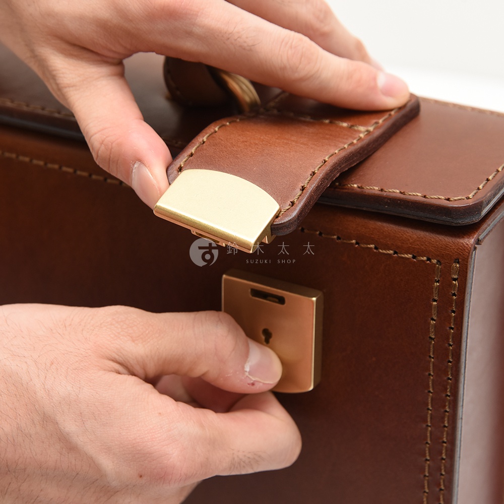 職人手作皮革兩用機師箱 BC-31-H，特寫箱蓋的皮革與黃銅色鎖扣，以及手部操作鎖頭的細節。