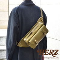 橄欖綠皮革騎士斜背包，配有銀色拉鍊和黃銅色扣環，展示於身穿深色外套的模特兒身上。