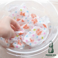 白色五層紗質地的擦拭巾，上面印有橘色蝴蝶和粉色、藍色、綠色圓點圖案，一隻手正在將其放入透明碗中。