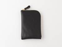 黑色皮革製成的職人手作迷你錢包，採用拉鍊開合設計，頂部有一個皮革拉環，縫線清晰可見，整體呈現簡約風格。