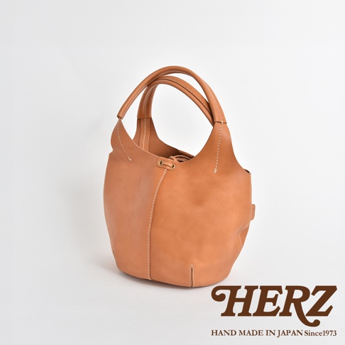 一款 tan 色皮革製成的球形肩掛托特包，包身線條流暢，採用縫線設計，配有雙提把，整體風格簡約。