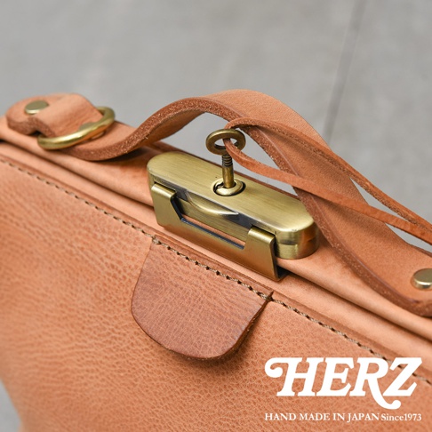 HERZ 職人手作皮革Organ鎖孔式大開口肩背包 M-7，特寫其古銅色鎖頭與鑰匙，搭配自然色澤的皮革紋理和縫線。