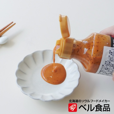 北海道芝麻擔擔風味沙拉醬從瓶中倒入精緻的白色醬料盤中，盤邊帶有花瓣狀的紋路，背景有筷子。