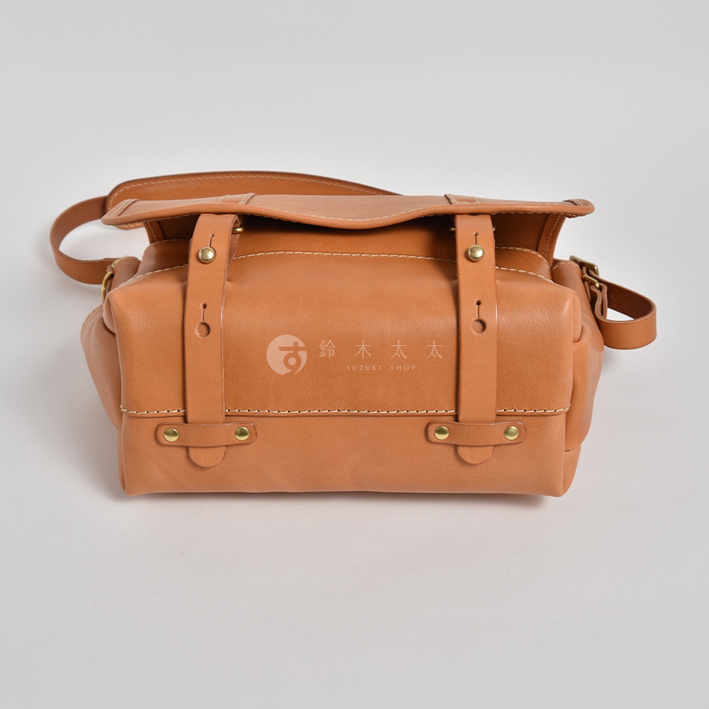 職人手作皮革復古郵差包，採用淺棕色皮革，配有金屬釦件和縫線細節，包款設計簡潔，附有可調式肩帶。
