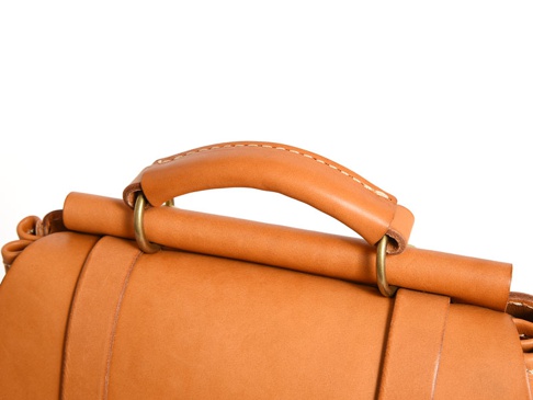 職人手作皮革屋瓦風經典雙扣後背包 (R-153) 的特寫，展示了棕褐色皮革提把、金屬環扣以及皮革包身細節。