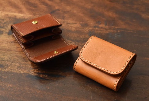 兩個皮革零錢包，一個淺棕色，一個深棕色，皆為雙折式設計，以白色縫線手工製作，並配有金色按扣。