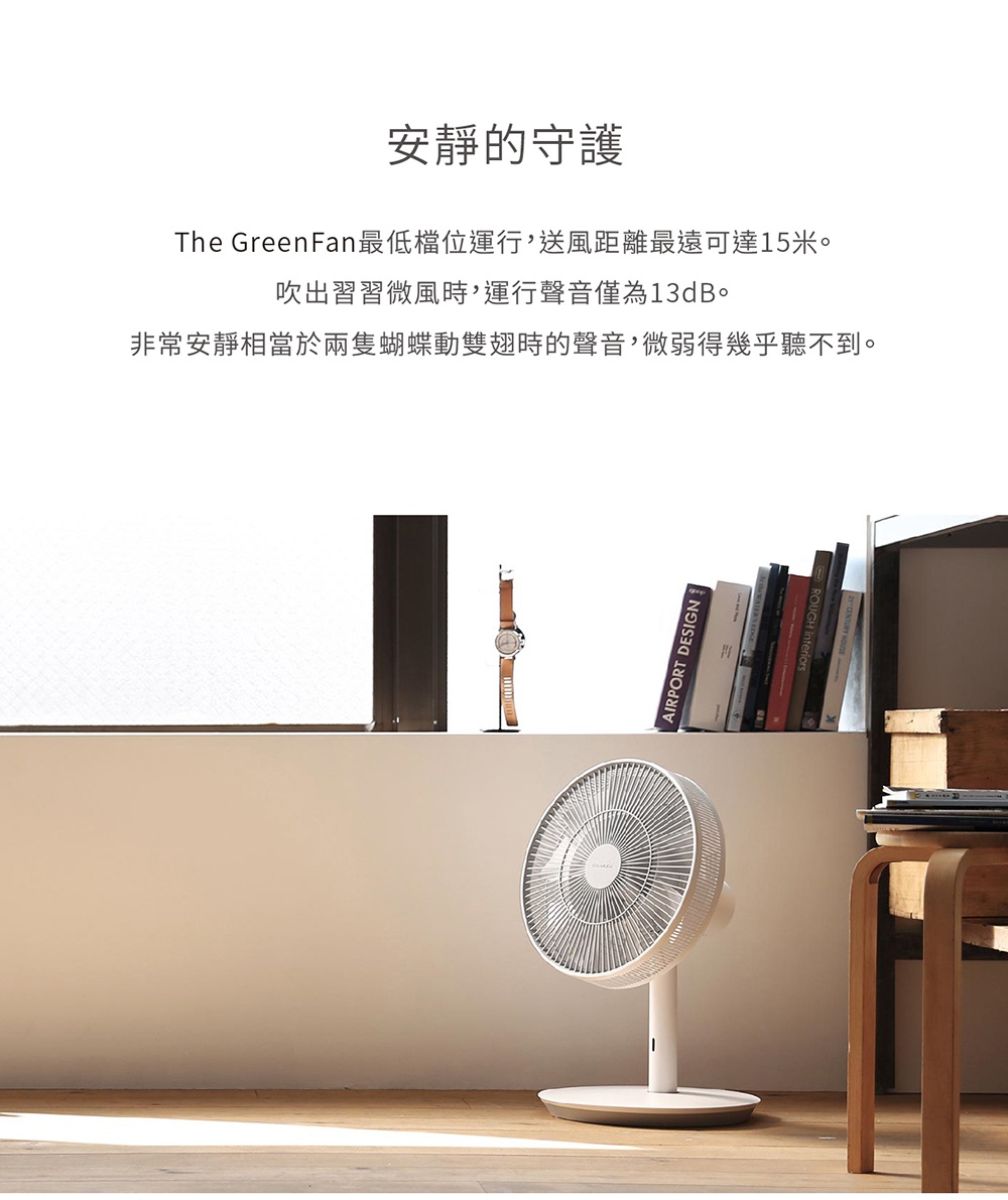 The GreenFan 風扇，白色扇葉與金色底座，簡約現代設計，置於地板上，背景有書籍與窗戶。
