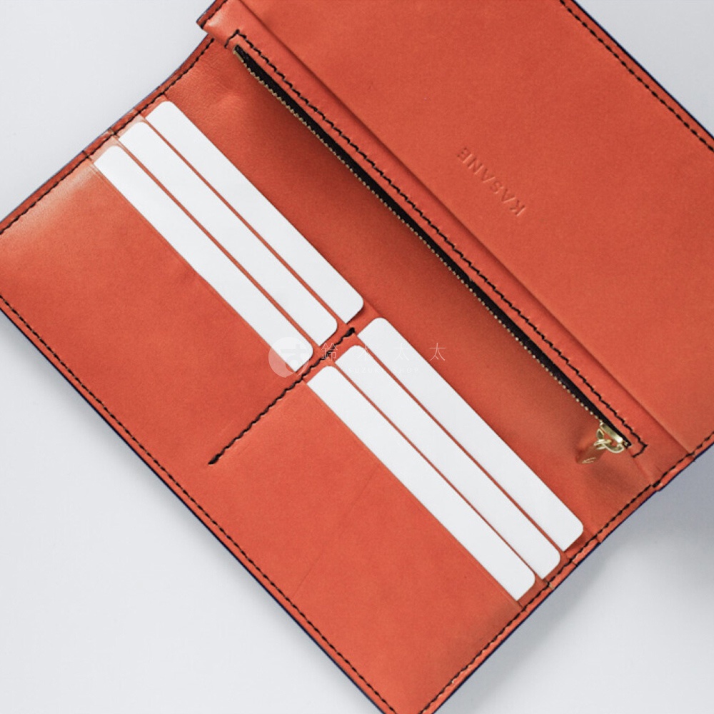 露出 KASANE 字樣的比利時 Rugato 皮革長夾內部，橘棕色內裡與卡片夾層，以及金色拉鍊的零錢袋。