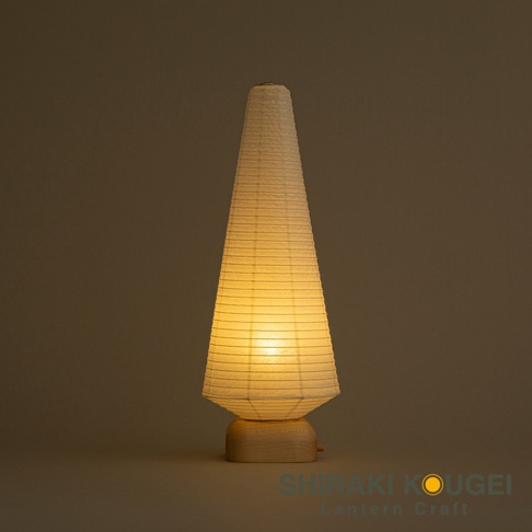 一個由白色紙張製成的錐形提燈，底部是淺木色底座，燈光從內部發出，營造溫暖的光暈。