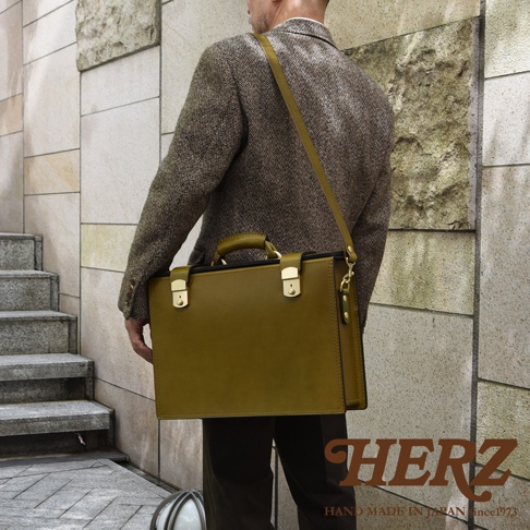 橄欖綠色皮革製成的職人手作兩用機師箱，配有金色鎖扣和提把，可肩背或手提。