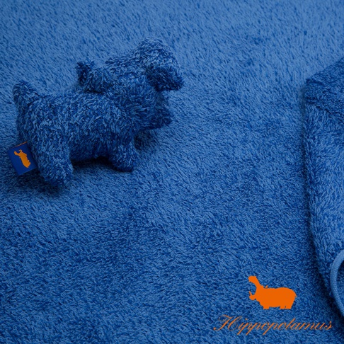 藍色竹棉混紡厚浴巾，質地柔軟，表面有毛圈紋理。左側有一隻藍色河馬造型的毛巾掛飾，掛飾上縫有橘色品牌標籤。右側可見浴巾邊緣及一條藍色綁繩。