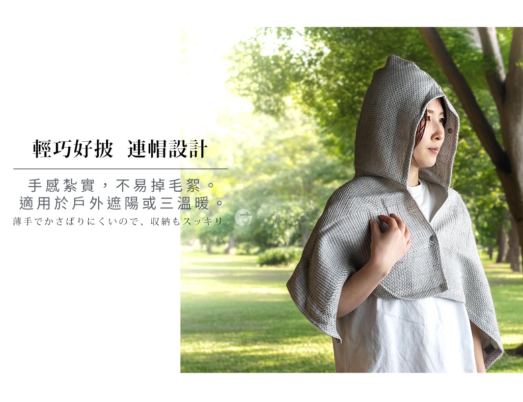 穿著一件灰色的連帽浴巾，左手扶著浴巾前端，背景是模糊的綠色樹林。