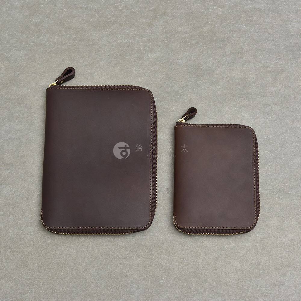 兩個深棕色皮革製的拉鍊收納包，大小不同，擺放在灰色背景上