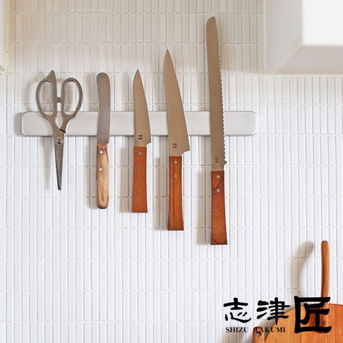 一組銀色金屬材質的廚房剪刀與四把刀，刀柄為木質，整齊地吸附在白色磁吸刀架上。