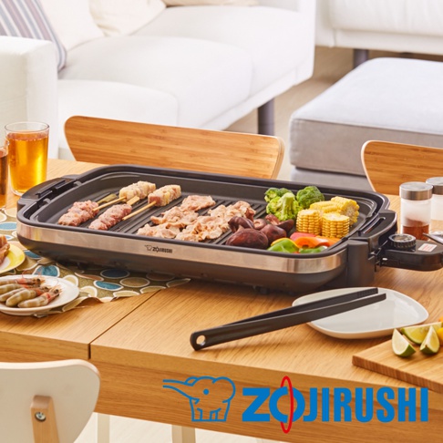 黑色分離式鐵板燒烤組，配有銀色邊框，內部烤盤上擺放著烤肉串、肉片、香菇、玉米、花椰菜和甜椒。