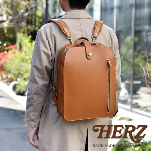 棕色皮革製成的雙肩後背包，背包頂部有提把和金屬釦，正面有一個拉鍊口袋，皮革縫線清晰可見。