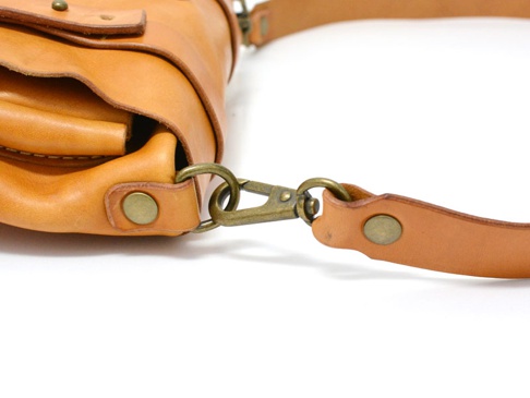 職人手作皮革水洗加工前雙口袋肩背包，淺棕色皮革，有金屬扣環與鉤扣，皮革邊緣有縫線與鉚釘裝飾。