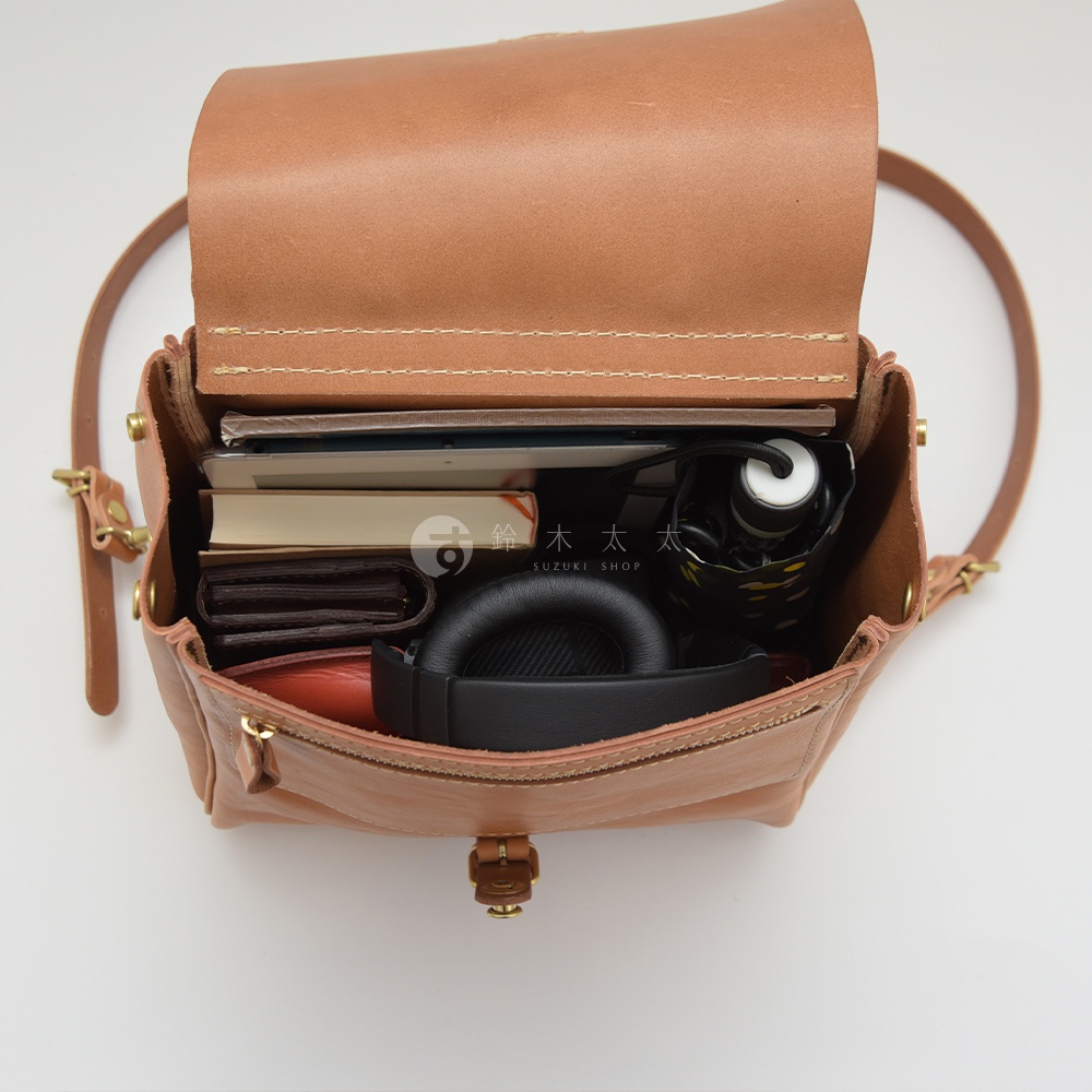 棕色皮革後背包，內含書籍、錢包、耳機和摺疊傘，展示背包的收納空間。