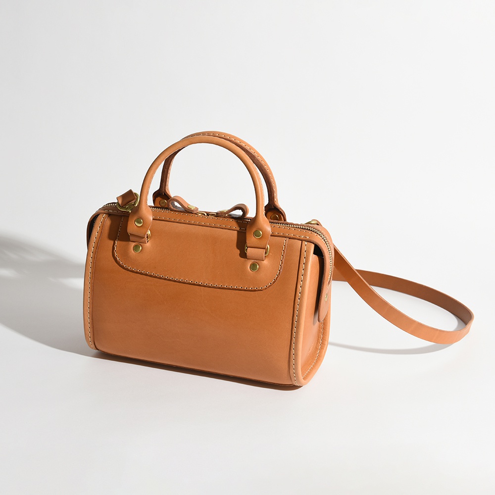 職人手作皮革迷你波士頓包，採用天然皮革材質，呈現溫潤的焦糖棕色，包身結構紮實，配有雙提把及可拆卸斜背帶，精緻縫線工藝。